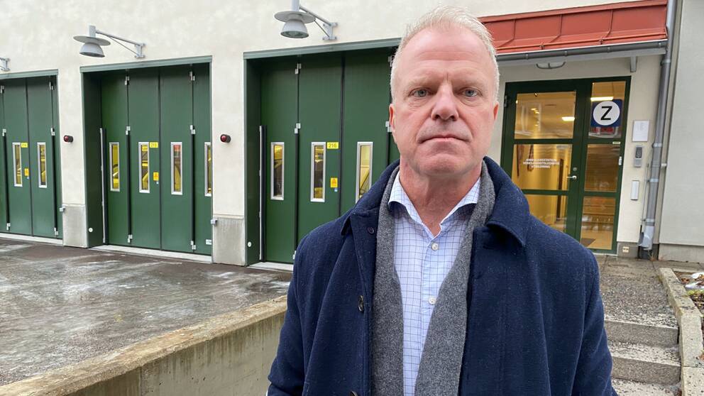 Fredrik Forselius, som är ambulanschef vid Region Dalarna och bär en blå rock, står framför ett ambulansgarage med gröna portar och berättar om det svåra personalläget.