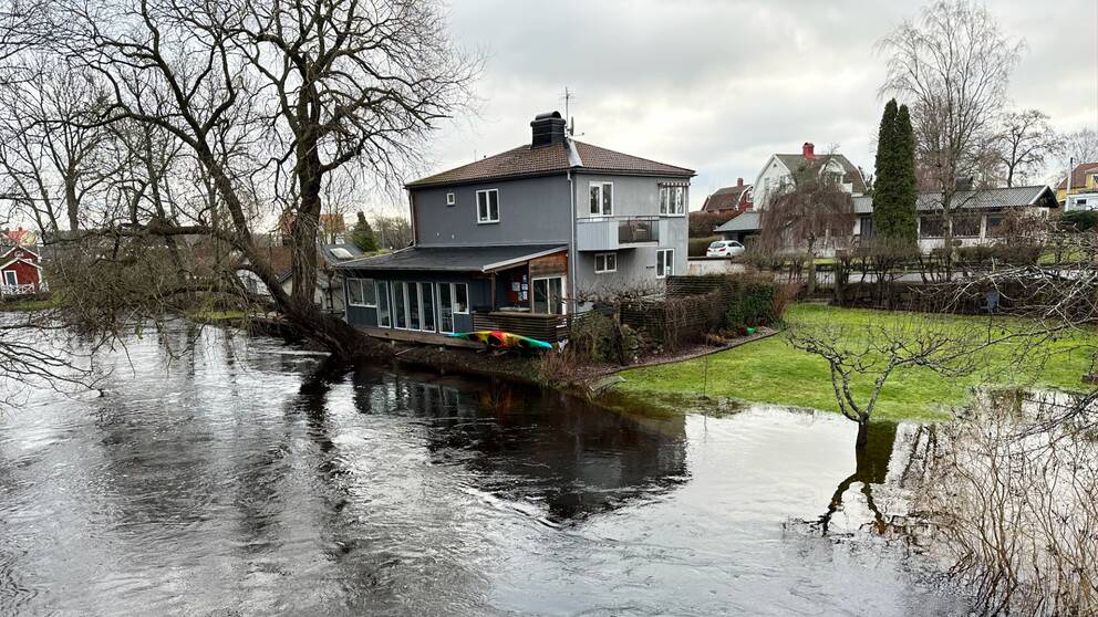 Ett grått hus ligger precis på randen till en övesvämmad å, Ljunbyån i Kalmar.