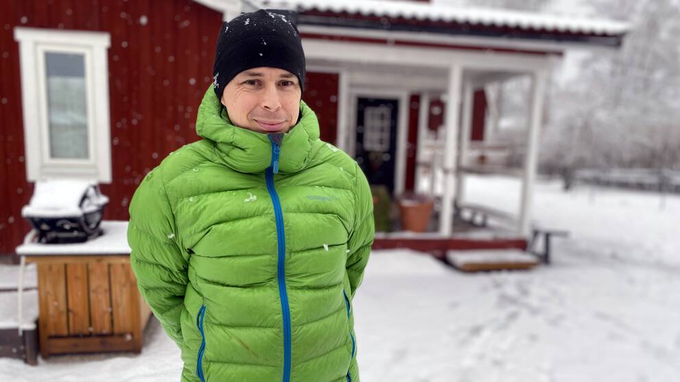 Sjuksköterskan Henrik Karlsson i Leksand står framför sitt röda hus med vita knutar. Det snöar och är vinter.
