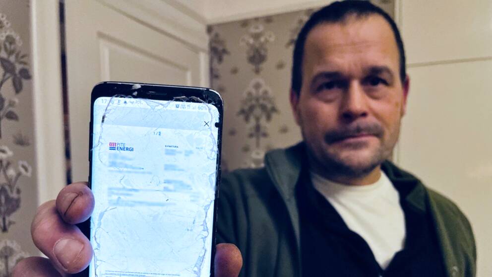 Thomas Burman – en man i grön fleece – håller upp sin telefon som visar familjens senaste elräkning.