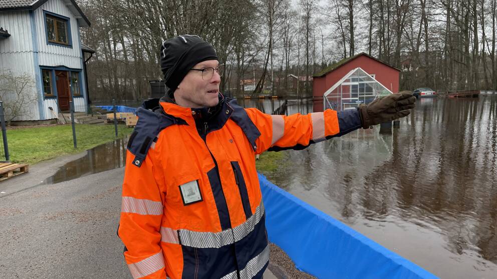 En man i skyddskläder pekar ut mot ett översvämmat område.