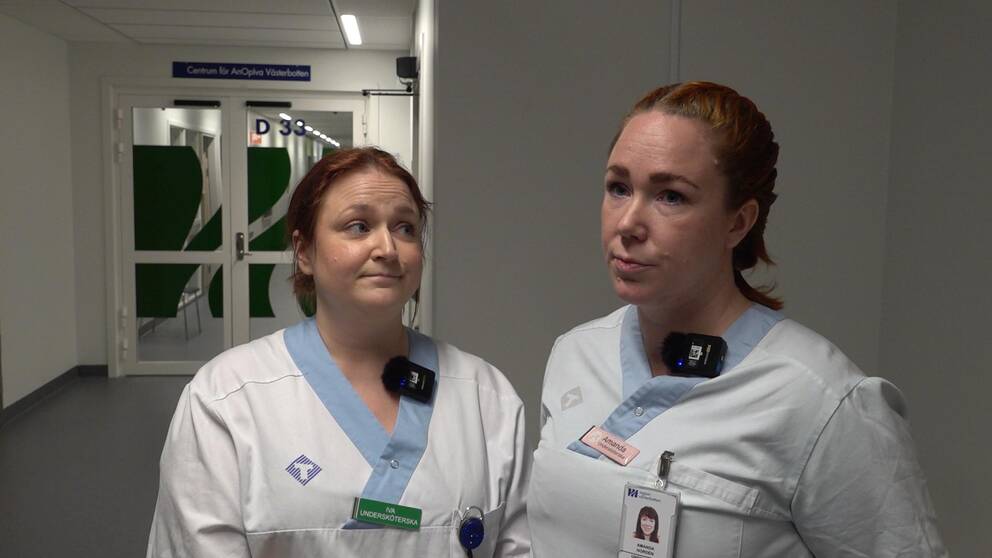 Två kvinnor iklädda sjukhuskläder står bredvid varandra i en sjukhusmiljö.