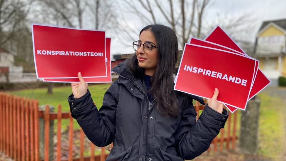 Kvinna med mörkt hår håller upp olika lappar. Hon heter Diba Dehnad och är reporter på SVT Nyheter Småland