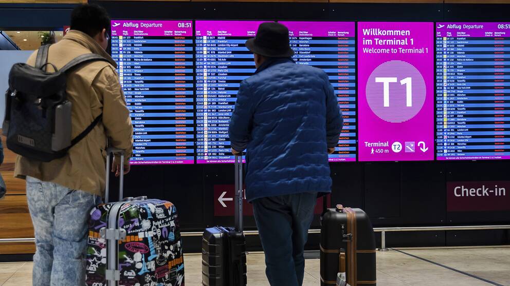 Två resenärer kollar på avgångsskyltar, där det står att alla flyg är inställda.