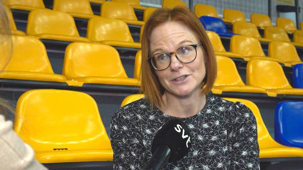 Camilla Olsson, kanslichef på Värmlands innebandyförbund, blir intervjuad när hon sitter på en läktare med gula och blå stolar i en sporthall.