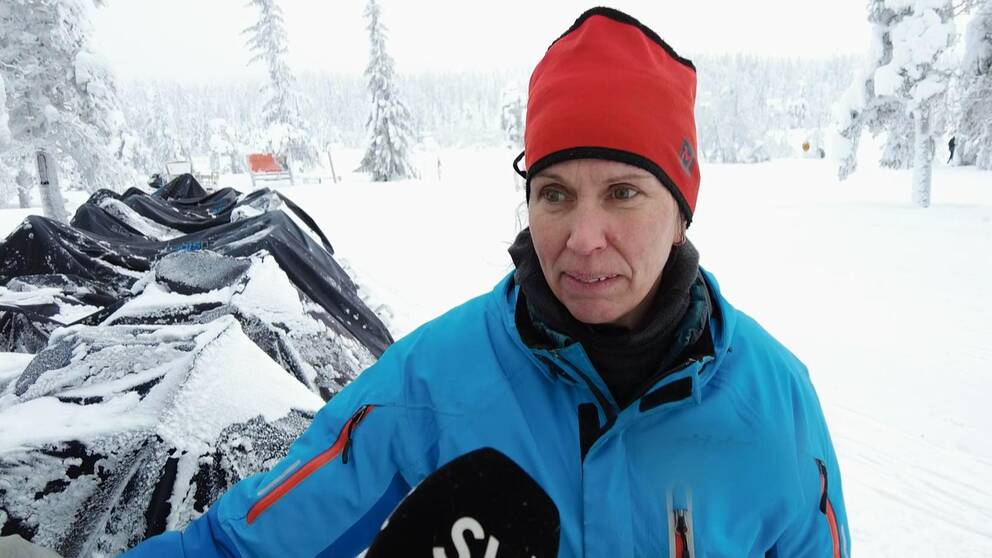 Kvinna i 45-årsåldern i röd mössa framför en rad övertäckta skotrar i vinterlandskap.