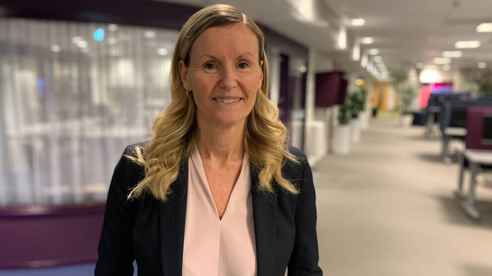 Linda Larsson, avdelningschef vid individ- och familjeomsorgen i Skellefteå kommun, står i ett öppet kontorslandskap. Hon har lockat långt blont hår och här klädd i en puderrosa blus med en svart kavaj över. 