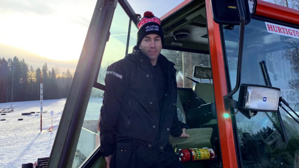 En man (Ordförande i skidklubben Hällefors SK Johan Ånger) står i dörren på en traktor/pistmaskin. Han är klädd i vinterkläder och det är soligt och snöigt bakom honom