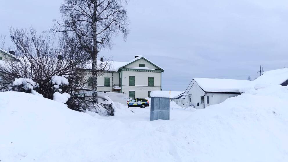 Vitt hus med gröna knutan och fönster i Gällivare. Framför huset syns en polisbil. Det är mycket snö. I förgrunden syns en björk och en snötäckt buske.