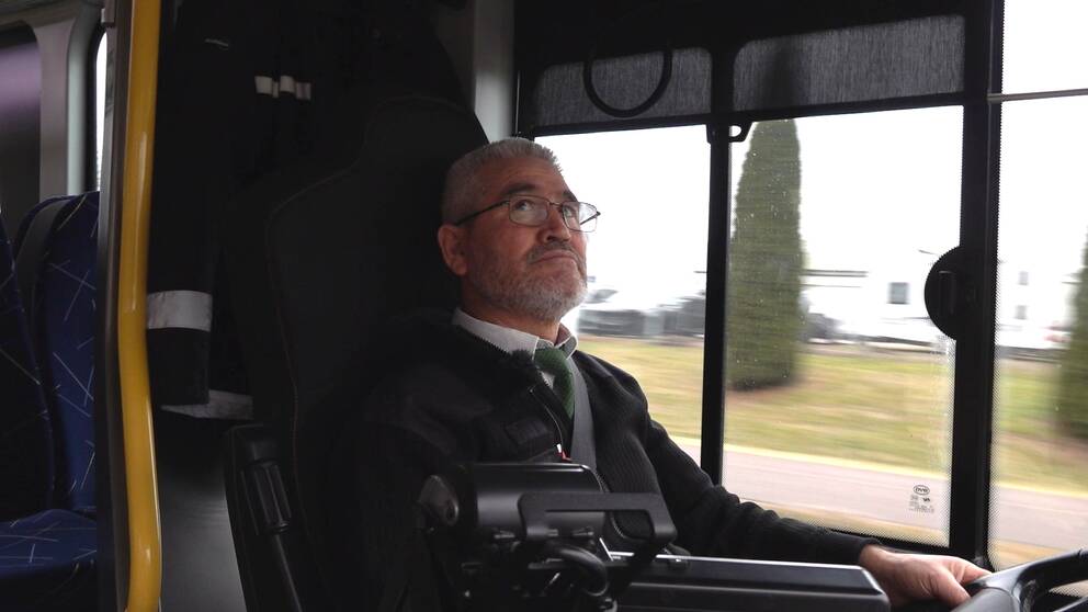 Busschauffören Sadeg sitter i förarsätet på en buss och tittar upp i backspegeln.