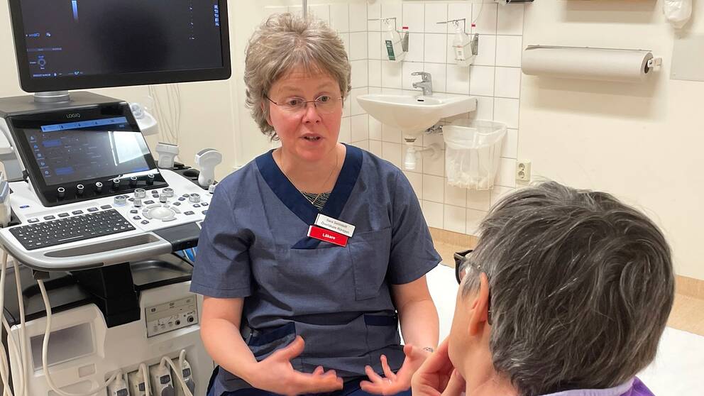 Sara Sehlstedt från Jämtlands läkareförening menar att arbetsmiljön inom vården är ett nationellt problem som måste åtgärdas. På bilden ser man Sara Sehlstedt klädd i mörkblå arbetskläder. Hon har grått hår och glasögon och sitter i ett undersökingsrum.