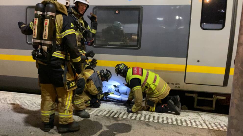 Brandmän som lyser med ficklampa under ett tåg.