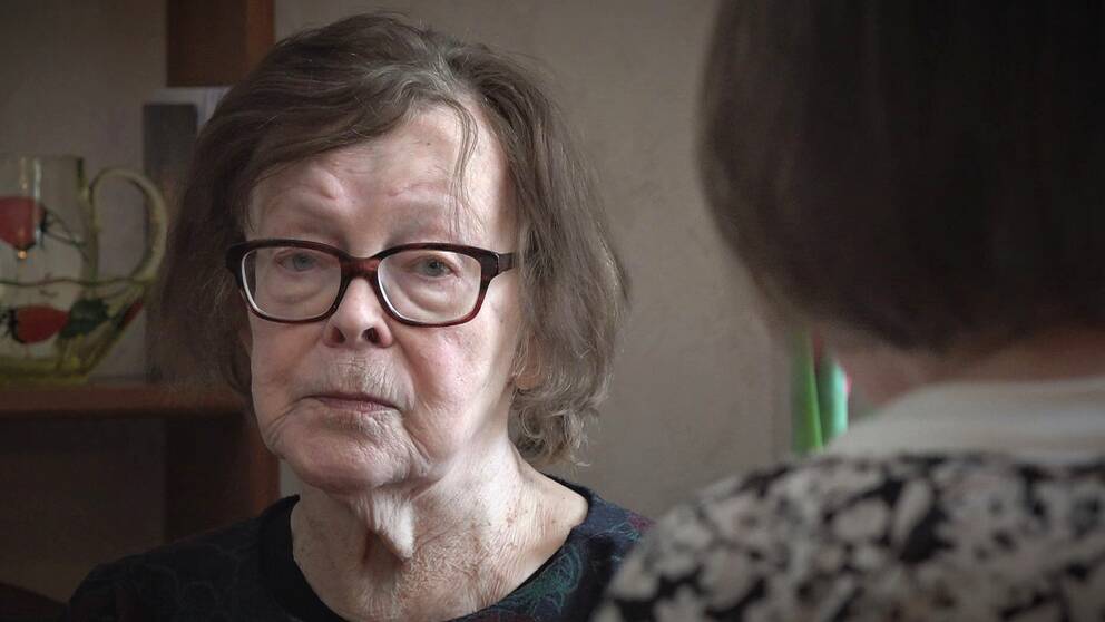 Äldre kvinna med glasögon och mörkt hår tittar uppgivet in i kameran.