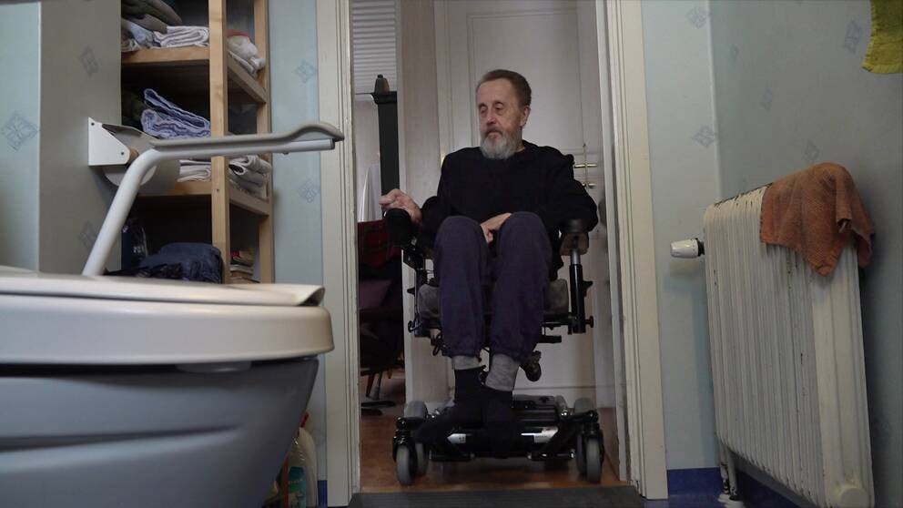 en äldre man i elektrisk rullstol tittar in i sitt lilla badrum