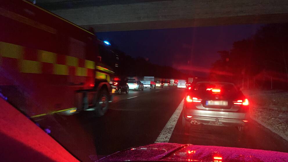 Bilar på en motorväg står stilla i en kö samtidigt som ett utryckningsfordon kör fram.