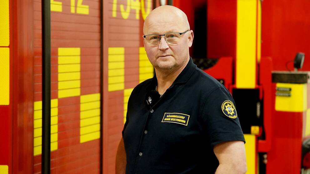 En man i pikétröja med räddningstjänstemblem står bredvid en brandbil.