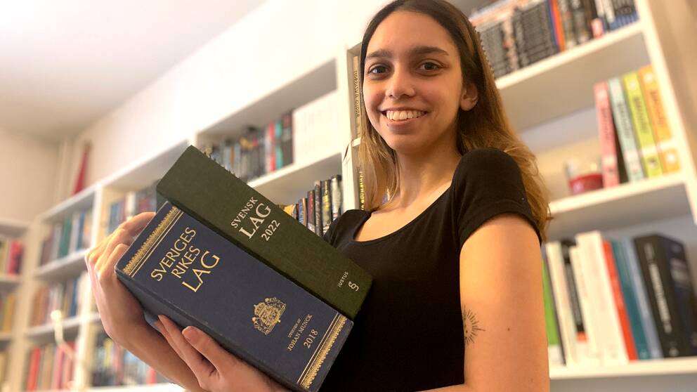 Mathilda Bandarian, tidigare den yngsta juriststudenten på juridiska institutionen, har tagit examen och håller upp två av Sveriges lagböcker.
