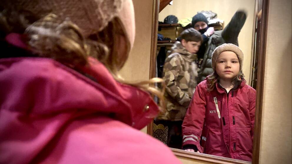 En familj under morgonen på väg ut, medan föräldern och ett barn tar på sig kläderna står dottern och tittar sig i hallspegeln.