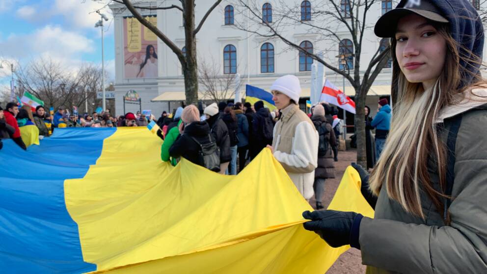 Människor utanför Stora teatern i Göteborg håller i en stor ukrainsk flagga. En tjej tittar in i kameran.