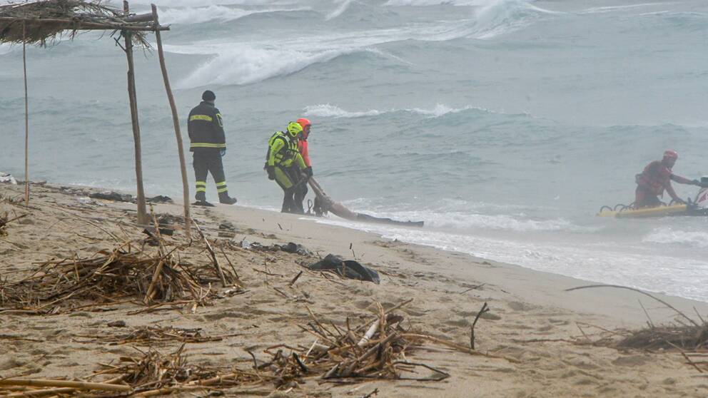 En person dras upp på stranden av italiensk räddningstjänst. På havet går det stora vågor.