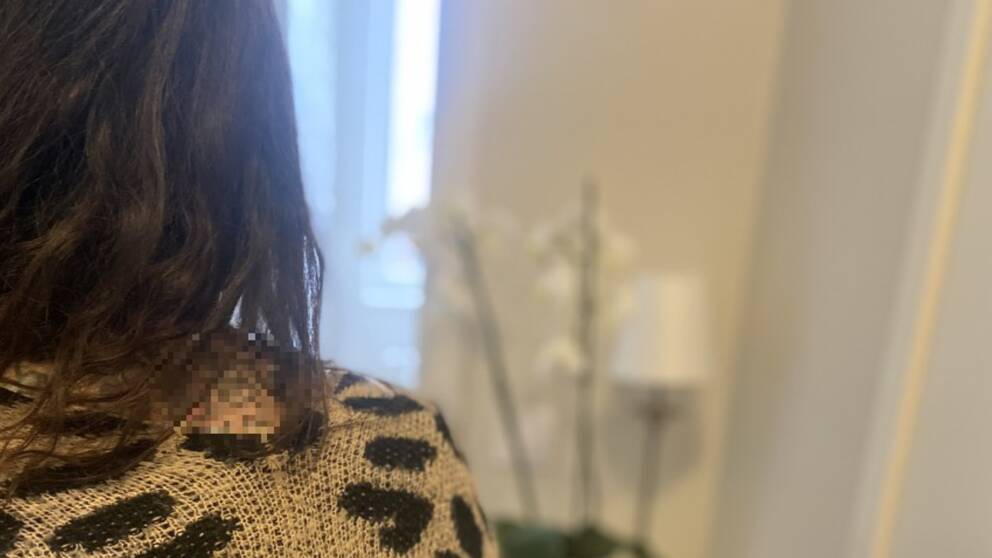 En person bakifrån, vi ser mörkt hår och en vit blomma i bakgrunden.