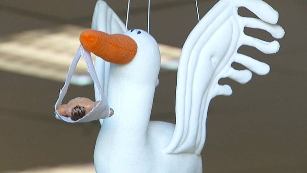 Bild på ett mjukisdjur föreställande en stork. I näbben hänger en docka. Ska symbolisera födsel.