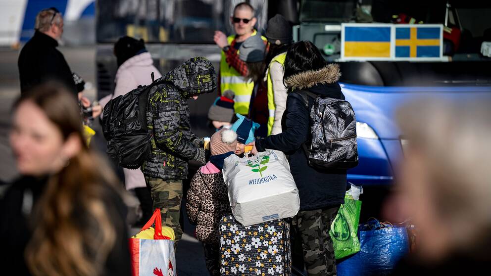 Människor som flytt från Ukraina står vid en buss i Karlskrona, en ukrainsk och en svensk flagga syns i fönstret på bussen. 