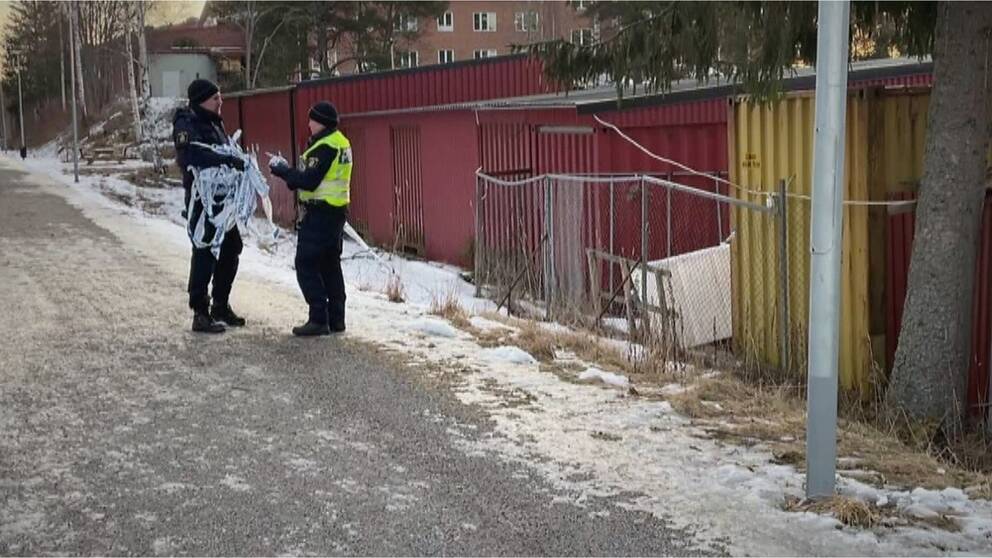 Två polisen står och samtalar på en liten grusväg. Den ene håller avspärrningsband i handen.