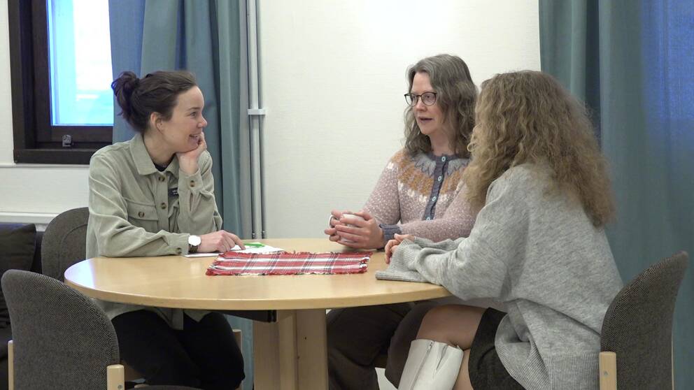 Tre kvinnor sitter runt ett bord och pratar