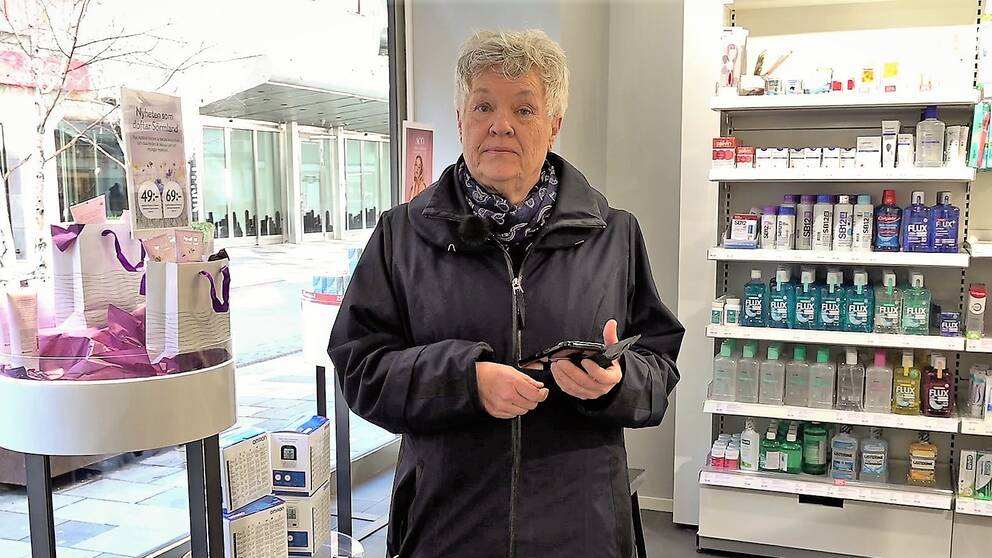 En äldre kvinna i ett apotek och med en mobiltelefon i handen.