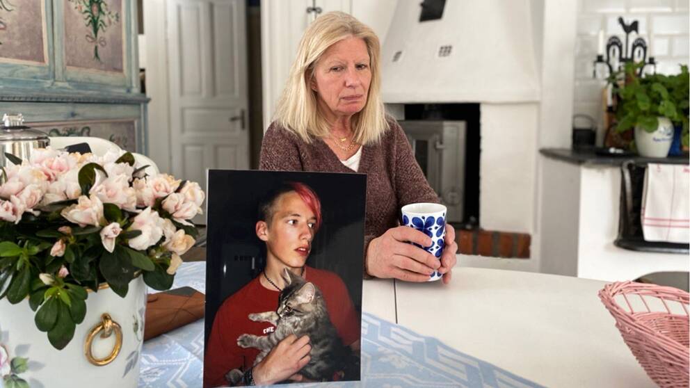En kvinna sitter med en kopp kaffe och tittar ner på ett foto av sin son.