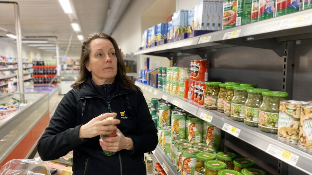 Bild på kvinna framför butikshylla med konserver och glasburkar. Kvinnan heter Annica Mattisson och är lanthandlare i Hällevik.