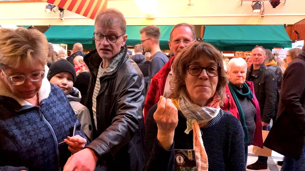 Människor står på en matfestival inomhus i Halmstad, pekar, provsmakar och tittar runt.