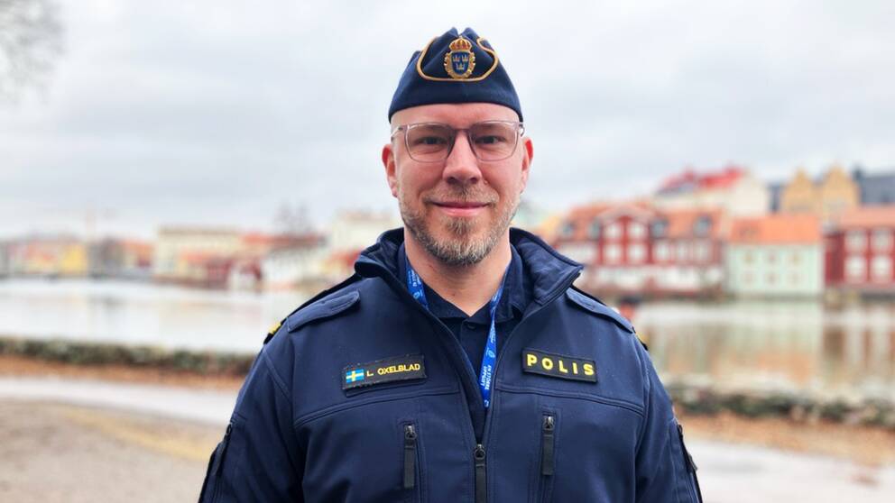 Bild på en manlig polis i uniform som står framför ett vattendrag och hus. Mannen heter Libbie Oxelblad och är Sörmlandspolisens attraherasamordnare. Han hoppas att distansutbildningen ska locka fler till polisyrket. 