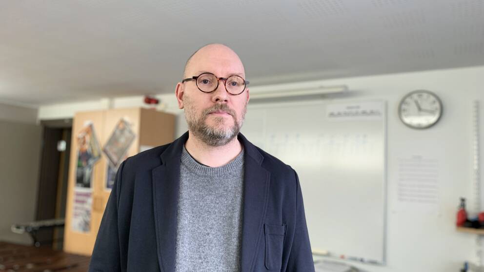 Kulturskolechefen Mikael Källarsson står i ett undervisningsrum med instrument framför en whiteboard.