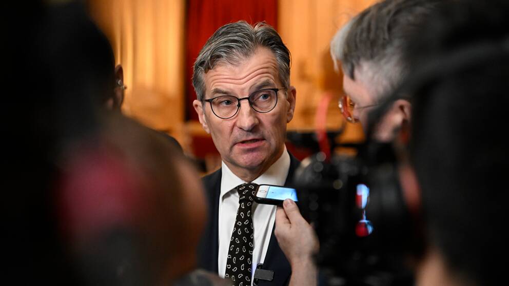 Bild föreställande riksbankchefen Erik Thedéen som syns bakom flera journalister.