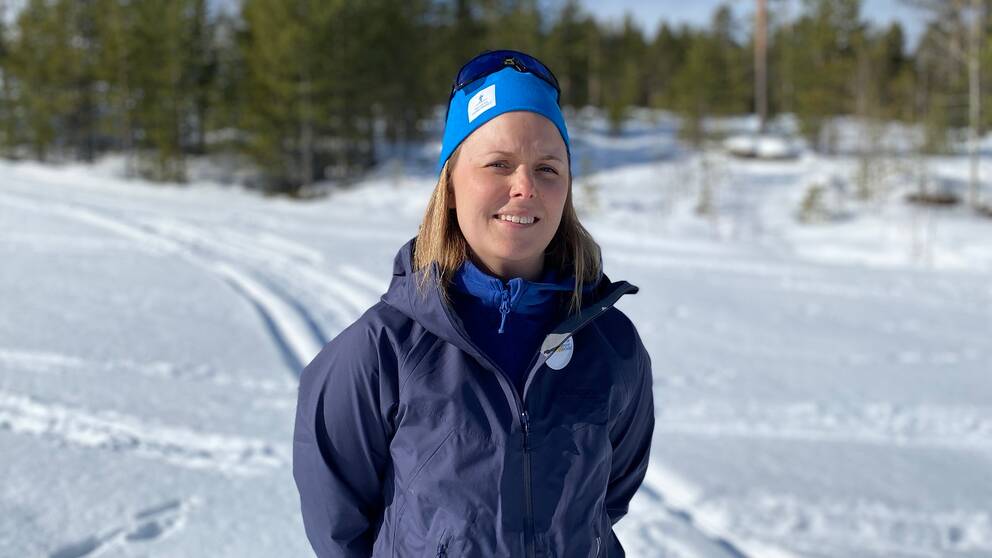 Blond kvinna i blå jacka och blå mössa, står i Hedebacken i Hede, Härjedalen.