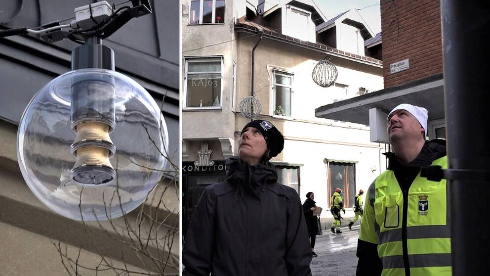 En kvinna med mörka kläder och en man med gulgrön jacka står i stadsmiljö och sneglar upp mot en gatlykta i form av en glasglob.