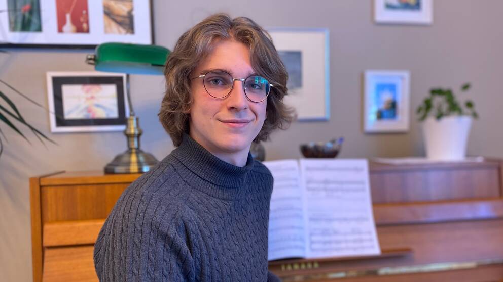 Milosz Krawczyk, en 19-årig kille med halvlångt hår och glasögon sitter framför ett piano med ett notblad och ler.