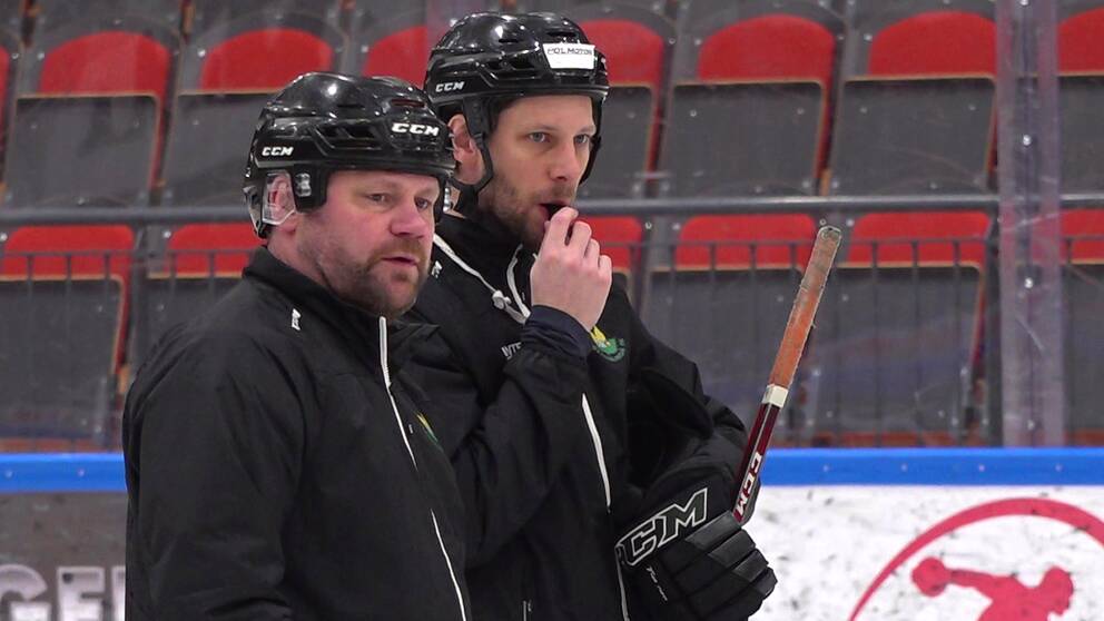 Kjell-Åke Andersson bredvid en annan man på en hockeyrink. De båda är klädda i svarta kläder och svarta hockeyhjälmar.