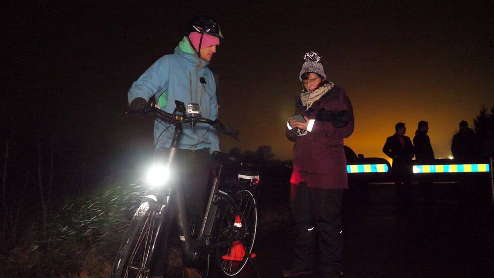 Simon Brohede i blå jacka, rosa mössa och cykelhjälm, får instruktioner av Anna-Maria Brohede från Högskolan i Skövde i lila jacka och toppluva inför testet med drönarbelyst cykelbana