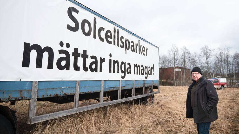 Lars-Gunnar Sandin står på åkermark vid sin stora uppsatta skylt där det står ”Solcellsparker mättar inga magar”. Nu ska skylten ner.