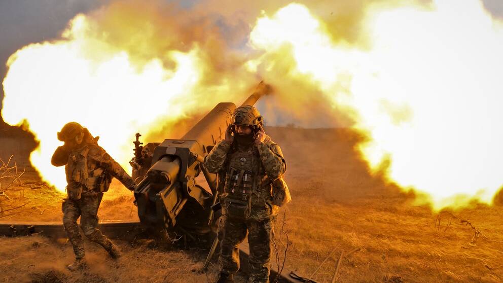 Soldater skjuter avfyrar en kanon på fronten. Ena håller för öronen. Det brinner och rök bildas.
