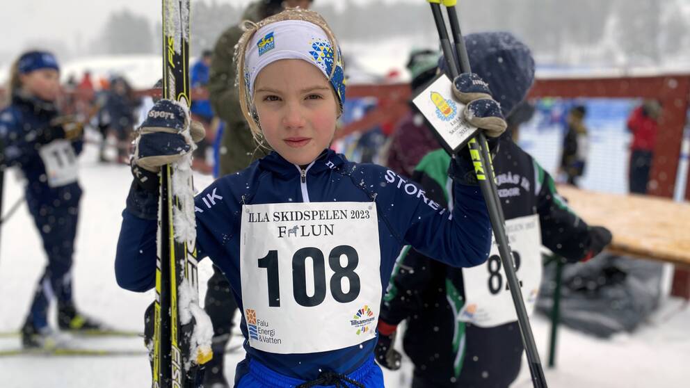 en ung flicka står med sina längdskidor och stavar i händerna i målområdet, det snöar