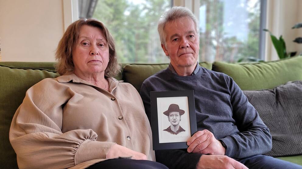 En kvinna och en man sitter i en soffa, mannen håller upp en bild på sin son Ola Bini. De är hans föräldrar.