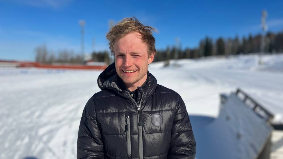 Björn Sandström, längdskidåkare står på Östersunds skidstadion och kisar i solen.