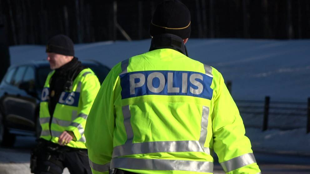 En ryggtavla av en polis i tjänst. Med en svart bil i bakgrunden.