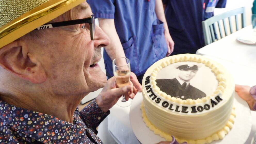 Olle Hernell med en partyhatt och en tårta där det står grattis olle 100 år.