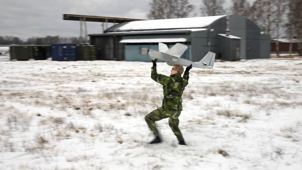 En person i kamouflageuniform kastar ett litet flygplan.