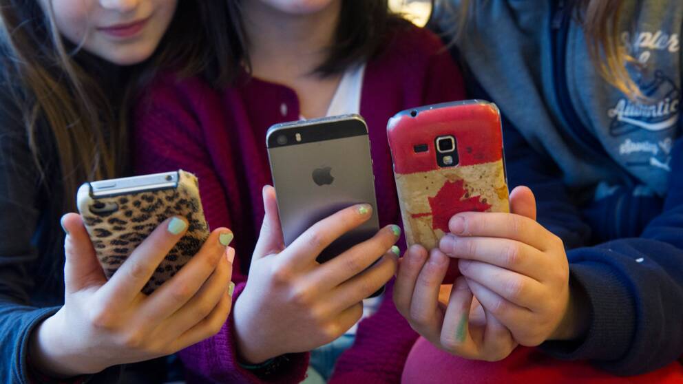 Tre flickor sitter och tittar på sina mobiler.